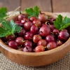 Rote Stachelbeeren in einer Holzschale mit frischen grünen Blättern.